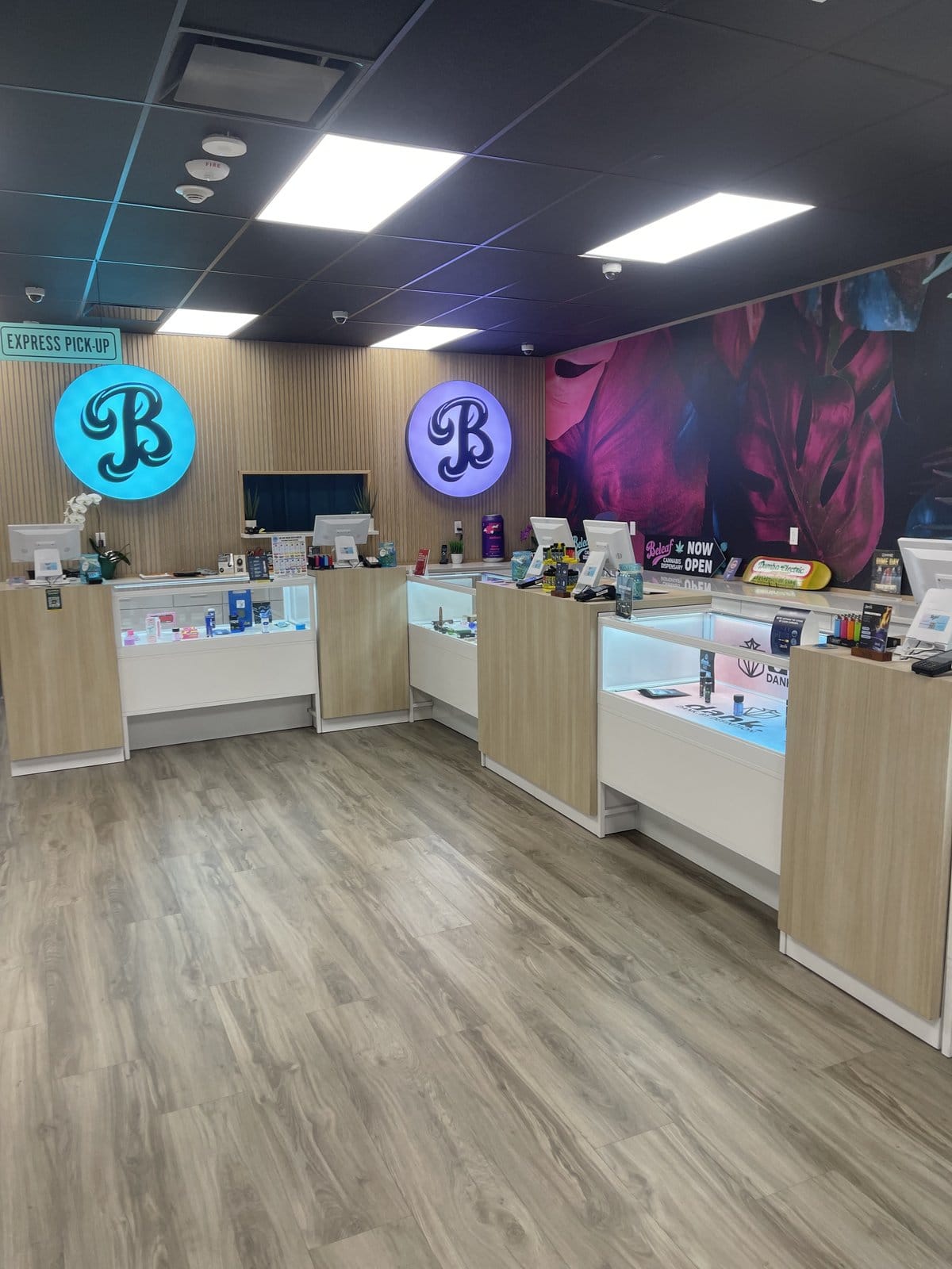Inside Beleaf Medford — illuminated teal and purple B logos over the express pickup counter with branded product displays