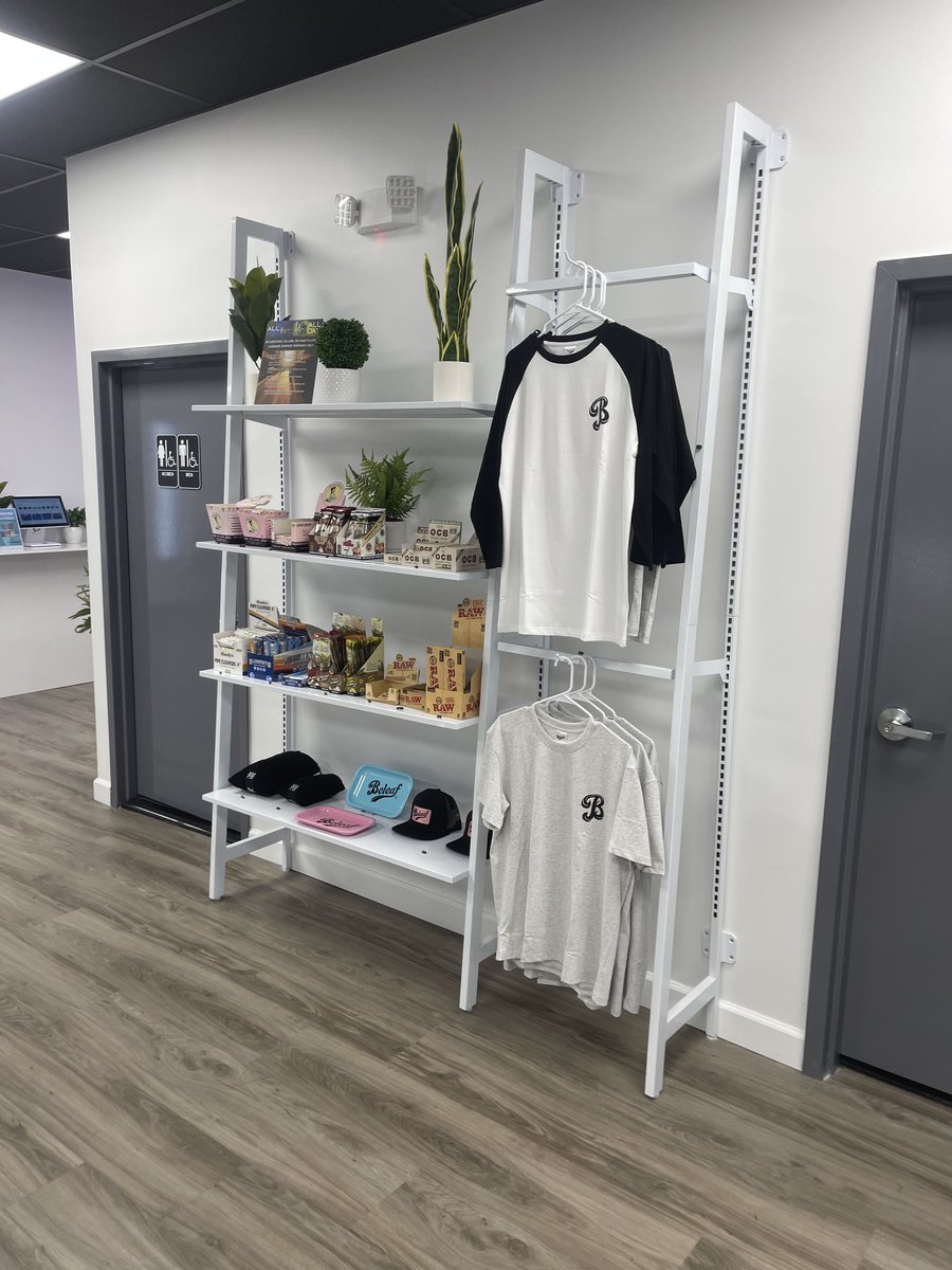 Beleaf branded merchandise rack at the Medford store - B-logo tees, hats, and rolling papers
